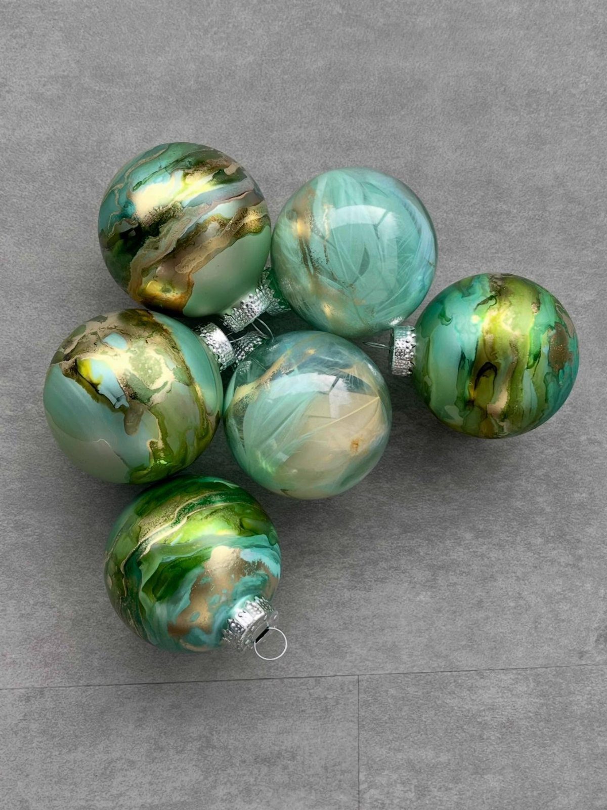 Cricut Christmas Balls: 14 DIY Ornaments for 2026 7 Six teal and gold painted glass Christmas ornaments resting on a grey textured surface.