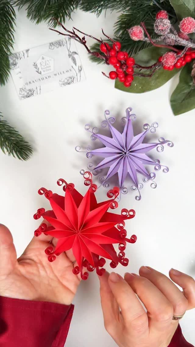 Cricut Christmas Balls: 14 DIY Ornaments for 2026 1 Hands holding two layered paper star ornaments in red and purple on a white background.