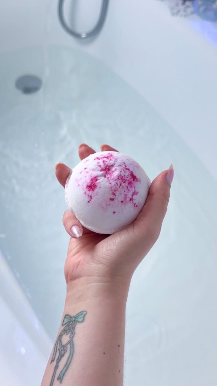 27 DIY Cheap Christmas Gifts for 2026 12 A hand holding a white bath bomb with pink speckles over a bathtub.