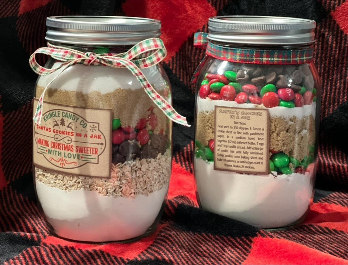 27 DIY Cheap Christmas Gifts for 2026 4 Two mason jars filled with layered cookie mix ingredients and colorful candies on plaid fabric.