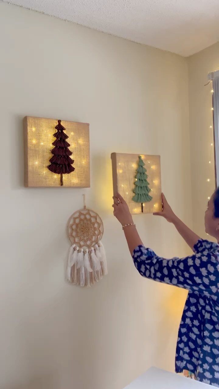 27 DIY Cheap Christmas Gifts for 2026 24 A person hangs a small canvas with a green tree design and lights on a wall.