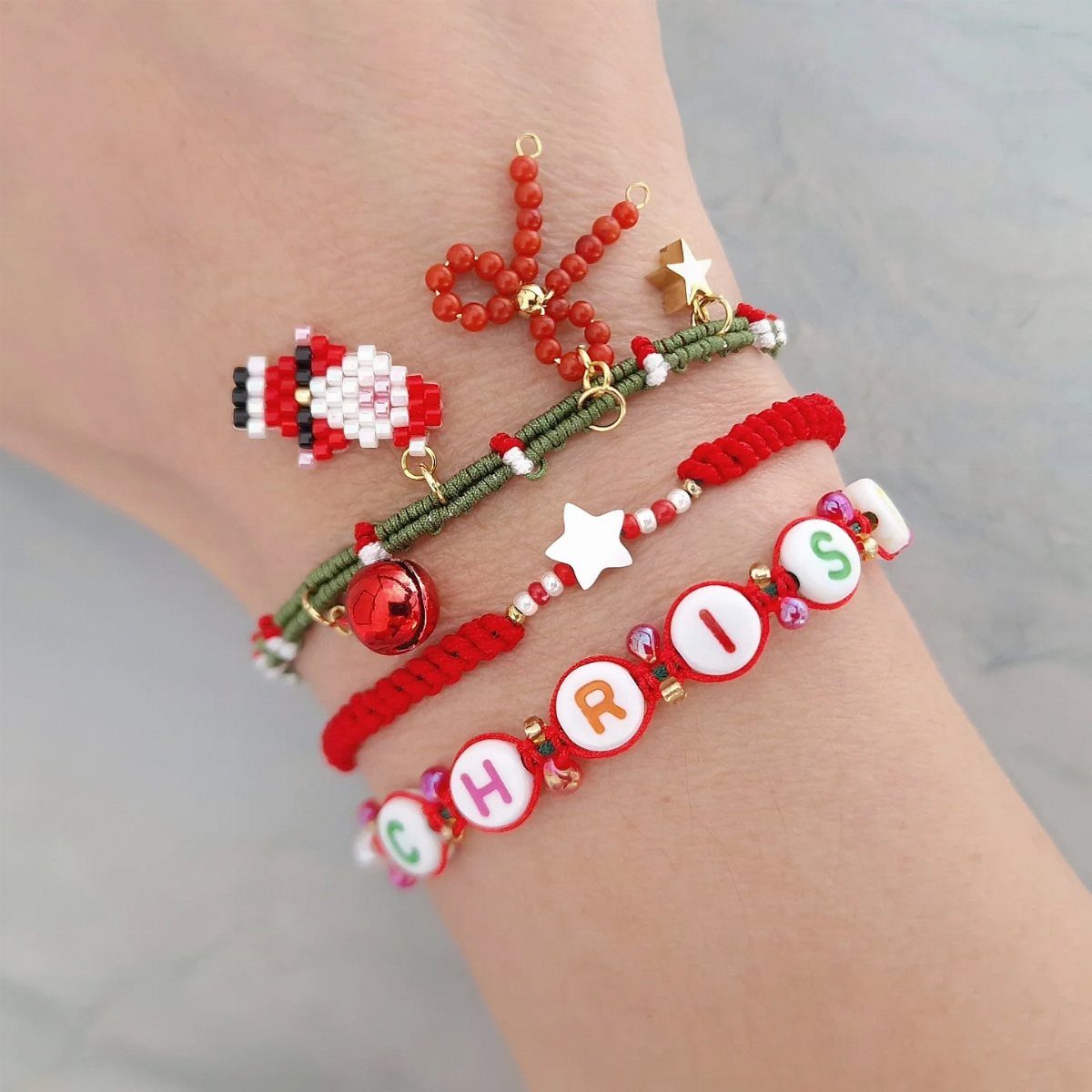 27 DIY Cheap Christmas Gifts for 2026 23 Handmade beaded bracelets with Christmas charms and letter beads worn on a person's wrist.
