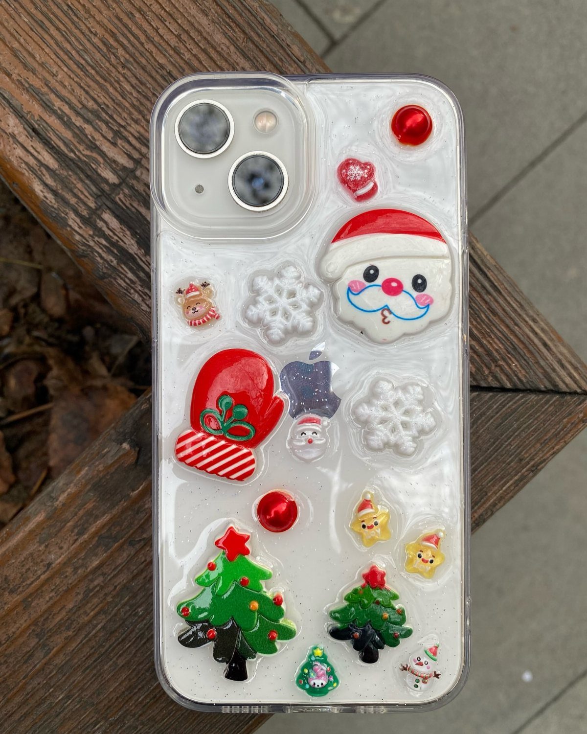 27 DIY Cheap Christmas Gifts for 2026 9 A clear phone case decorated with colorful Christmas charms like Santa, snowflakes, and trees.