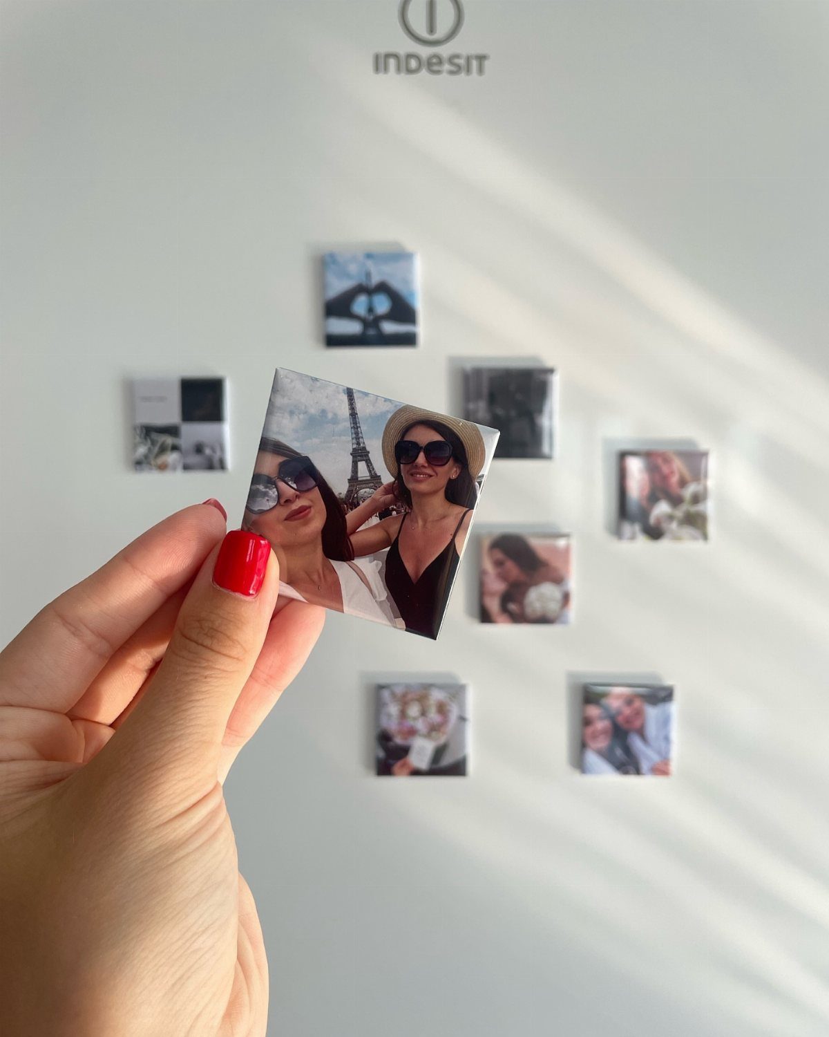 27 DIY Cheap Christmas Gifts for 2026 5 A hand holding a small square photo magnet against a white refrigerator background.