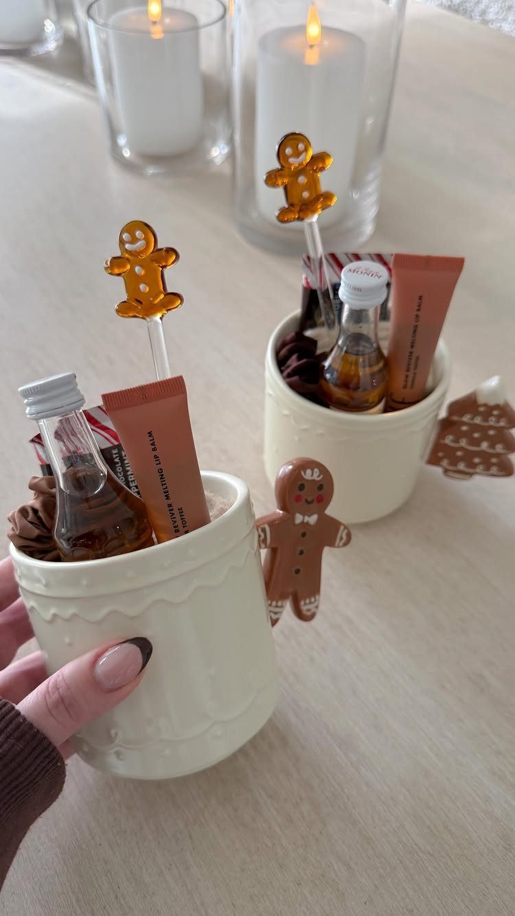 27 DIY Cheap Christmas Gifts for 2026 26 Two white mugs containing lip balm, small bottles, and gingerbread man decorations on a table.