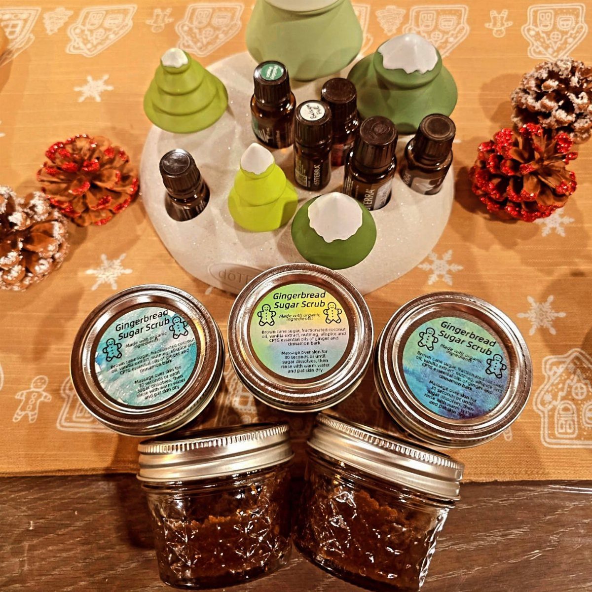 27 DIY Cheap Christmas Gifts for 2026 3 Four jars of gingerbread sugar scrub arranged with essential oils and decorative ceramic trees.