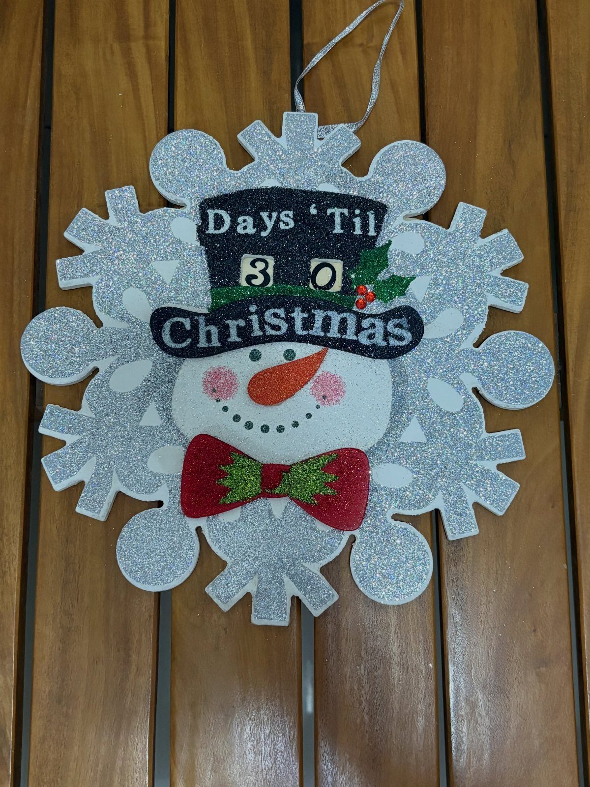 A glittery snowflake ornament with a snowman face and a countdown sign on its hat.