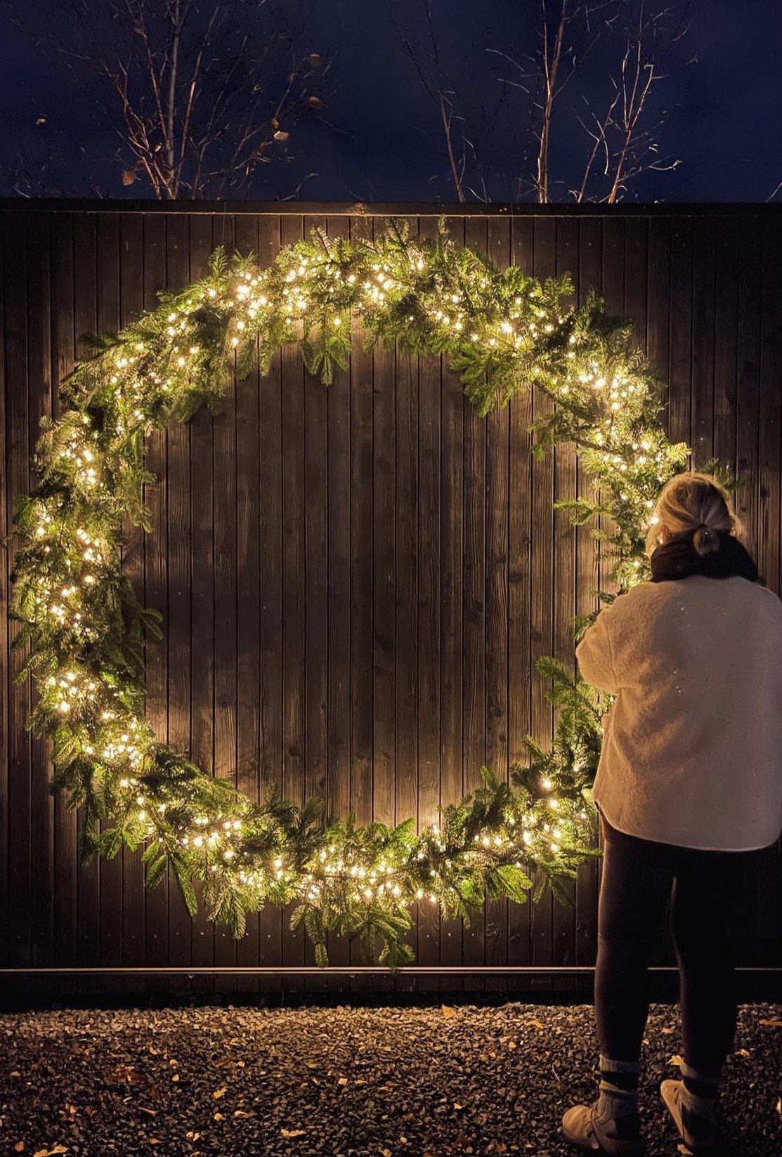 A large illuminated green garland hanging on a dark wooden fence at night.