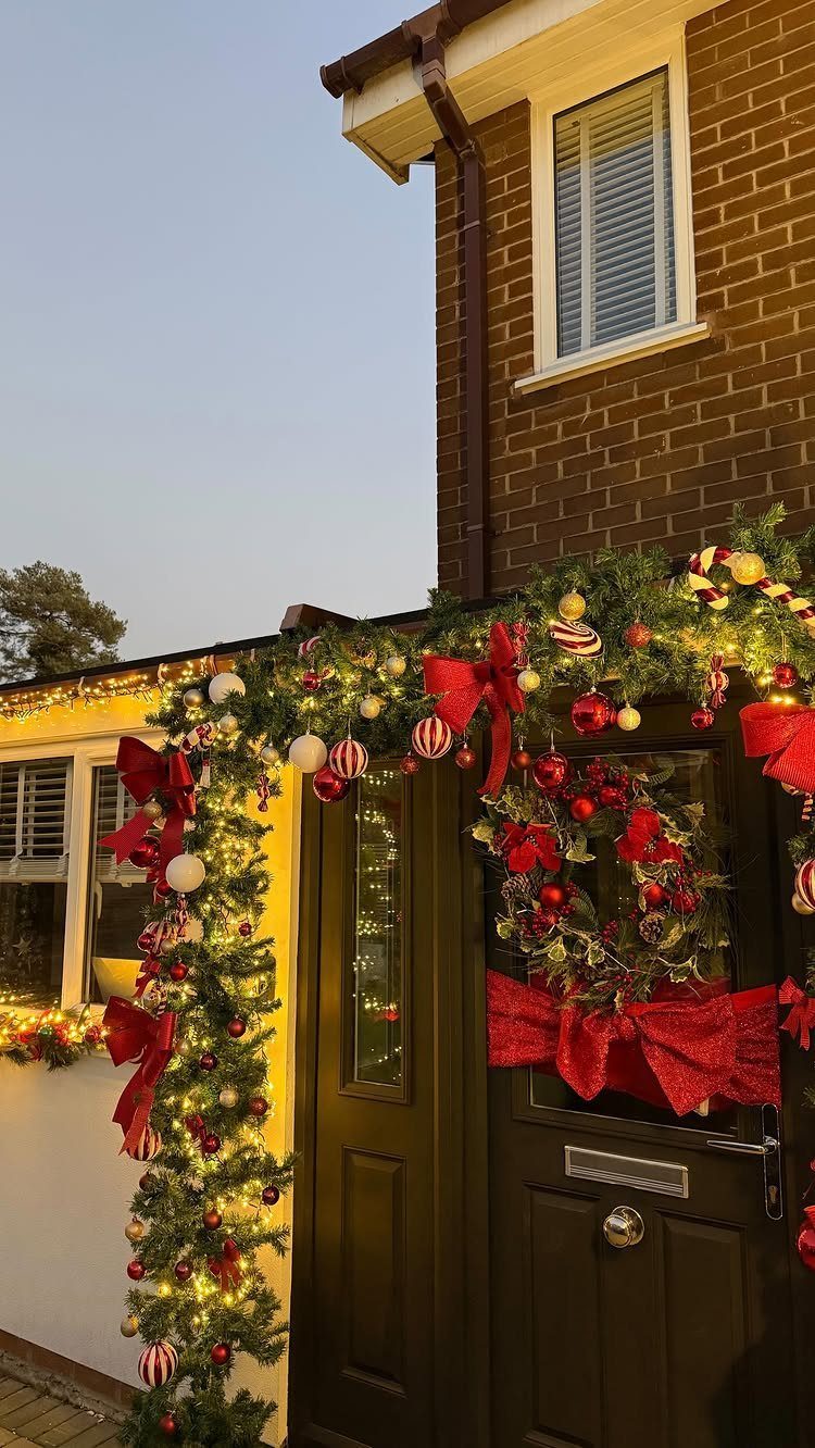 Green Christmas garland with red bows and lights decorating a dark wooden front door.