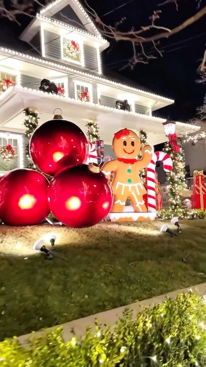 Large red ornaments and a gingerbread man stand on a lawn decorated with Christmas lights.