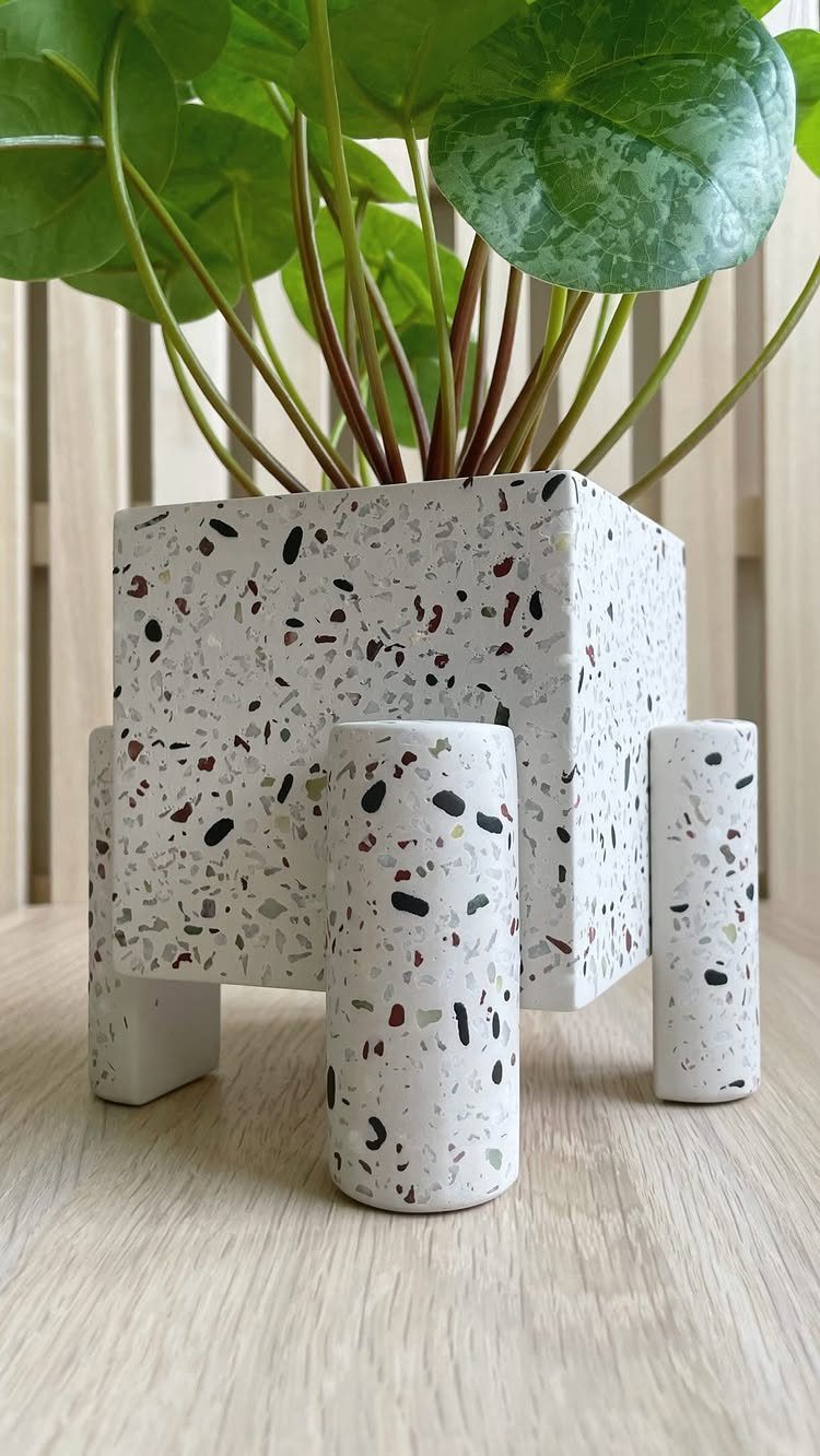 9 Easy DIY Planter Ideas for Wood, Upcycled & Clay Projects 7 A white terrazzo-patterned square planter with cylindrical legs containing a green plant with large leaves.