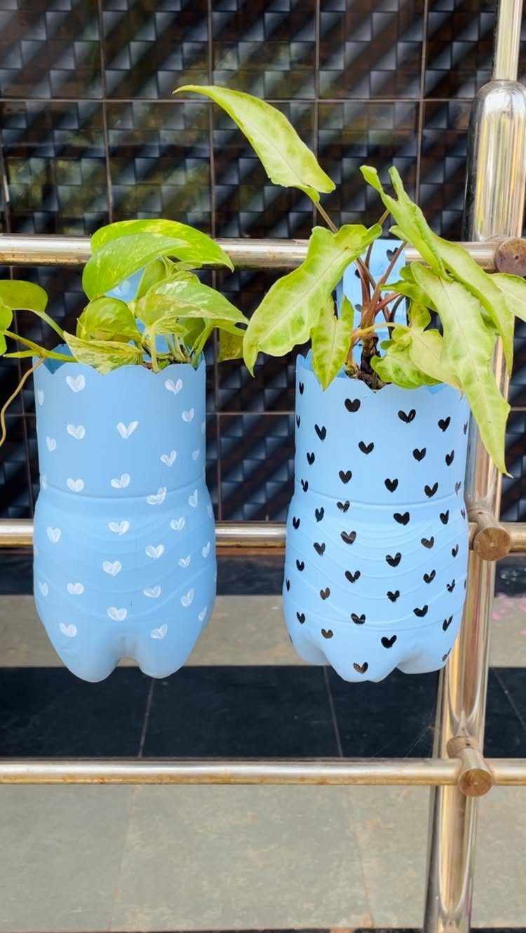 9 Easy DIY Planter Ideas for Wood, Upcycled & Clay Projects 5 Two blue plastic bottle planters with heart patterns containing green plants hanging on a metal rail.