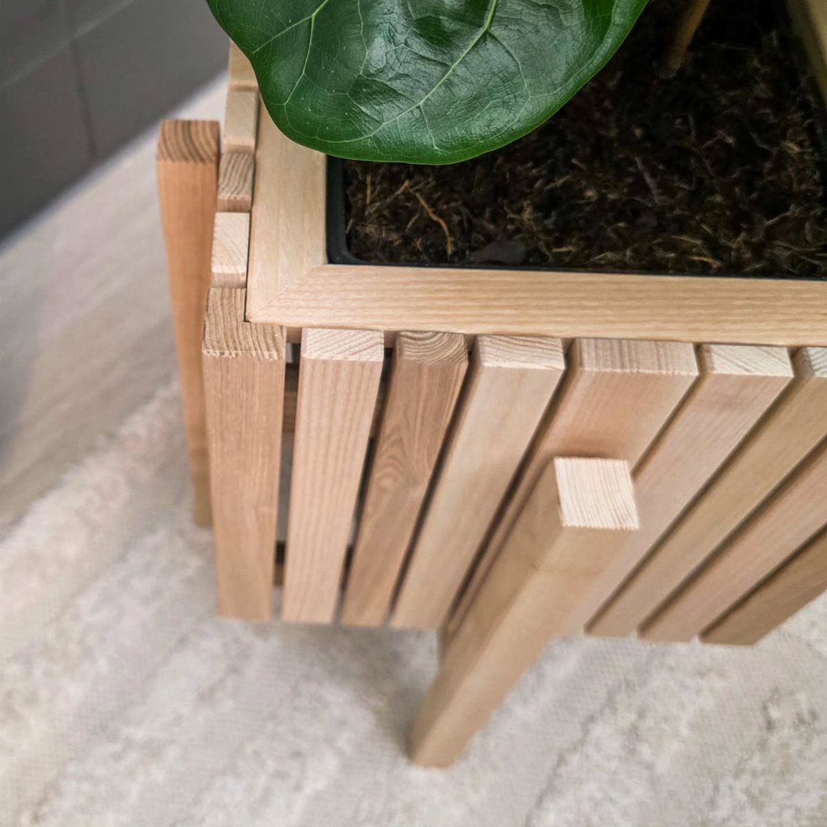 9 Easy DIY Planter Ideas for Wood, Upcycled & Clay Projects 2 A light wood slat planter with angled legs containing a green plant on a rug.