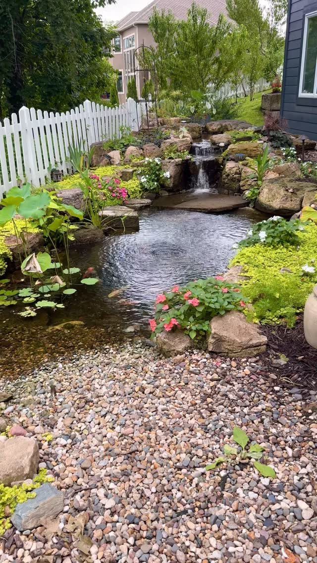 15 Huge Garden Design Ideas for Birds, Light, Night Paths and Still Water 13 A backyard garden with a stone waterfall flowing into a small pond surrounded by lush greenery.