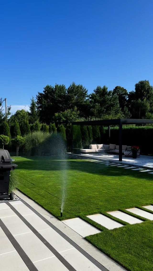 15 Huge Garden Design Ideas for Birds, Light, Night Paths and Still Water 14 Manicured green lawn with stepping stones, a pergola, and a water sprinkler under a blue sky.