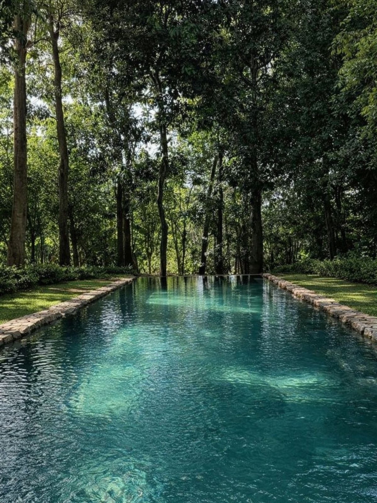 15 Huge Garden Design Ideas for Birds, Light, Night Paths and Still Water 8 A long rectangular reflecting pool with turquoise water surrounded by stone edges and tall green trees.