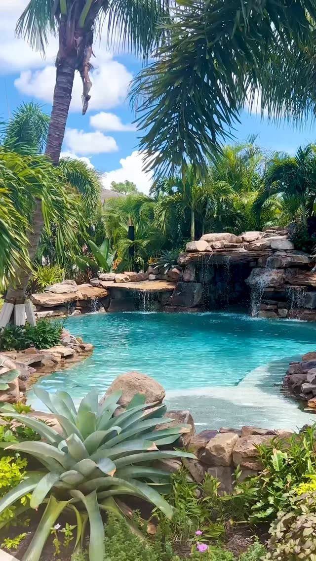 15 Huge Garden Design Ideas for Birds, Light, Night Paths and Still Water 11 Tropical swimming pool with a rock waterfall surrounded by lush palm trees and green vegetation.