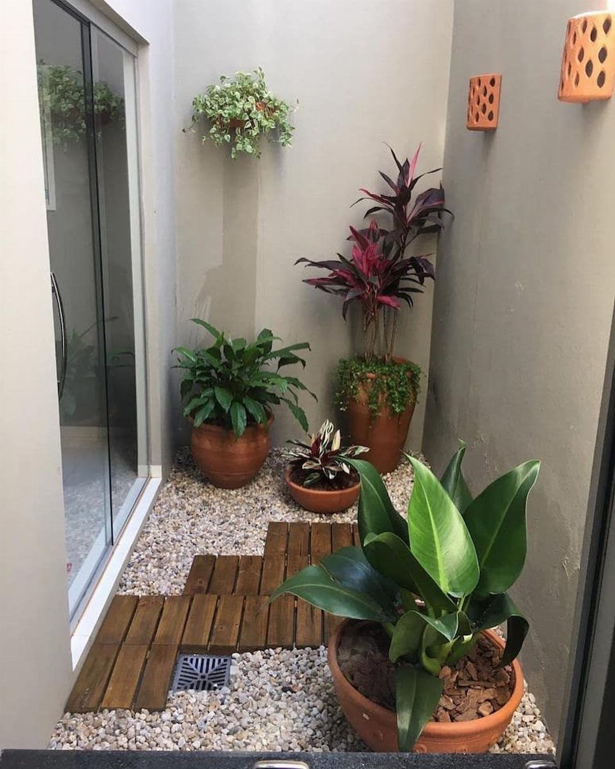 11 Indoor Green House Room Ideas for Every Budget 7 Potted tropical plants arranged on gravel with wooden stepping stones in a small indoor courtyard.