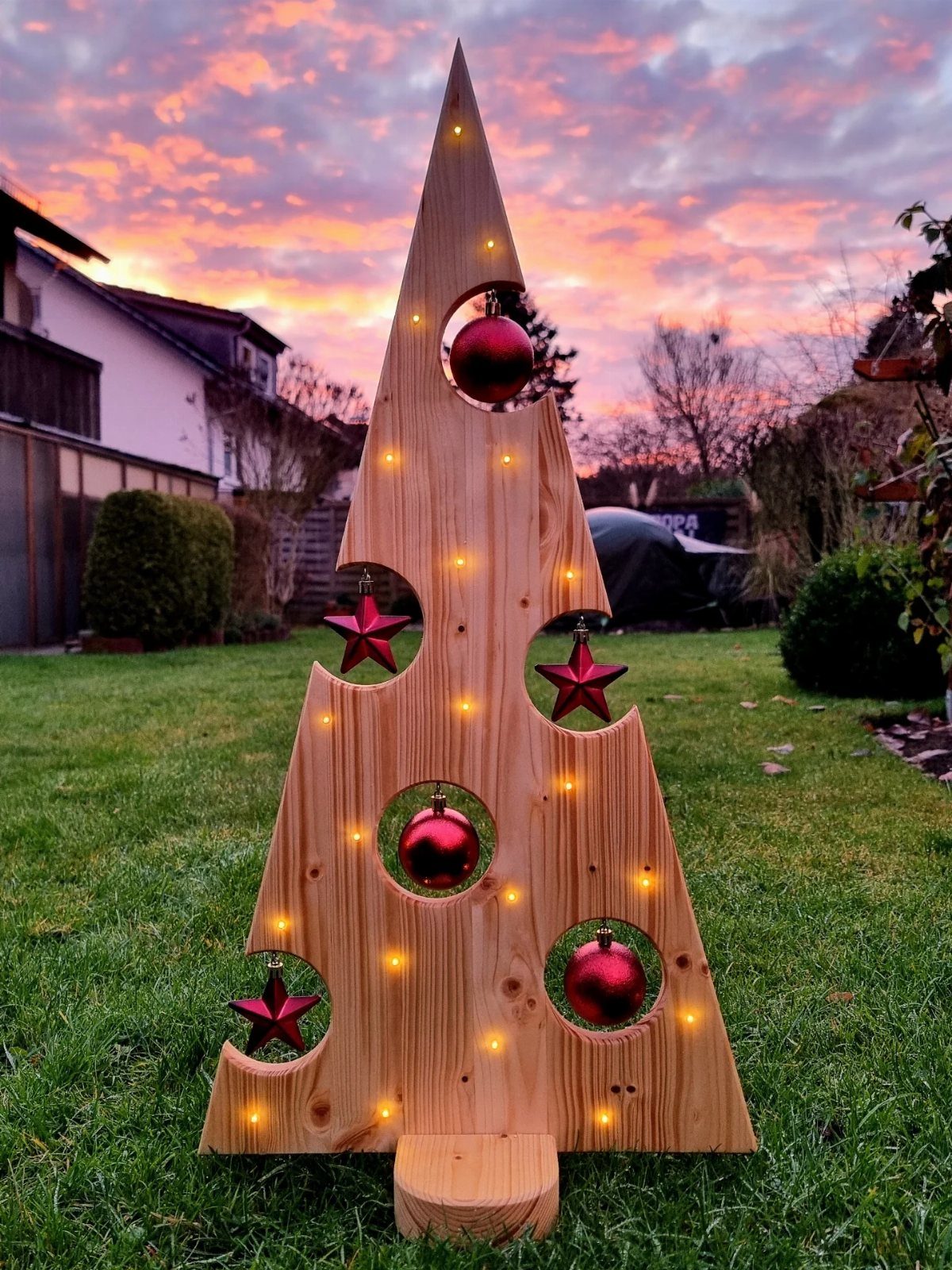 Make Wooden Christmas Trees: 7 DIY Projects from Scrap to Yard 2 A large wooden triangular Christmas tree with circular cutouts and lights standing on a lawn.