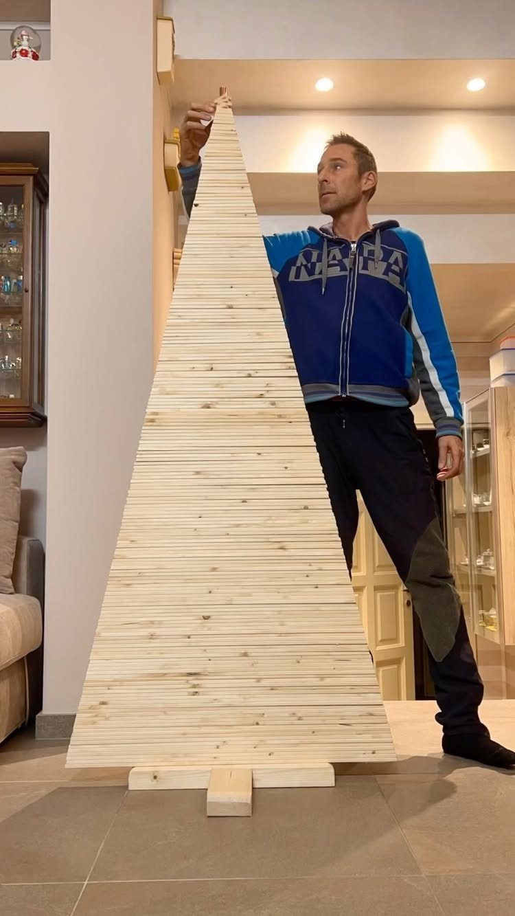 Make Wooden Christmas Trees: 7 DIY Projects from Scrap to Yard 5 A tall triangular wooden tree structure made of horizontal slats standing next to a man.