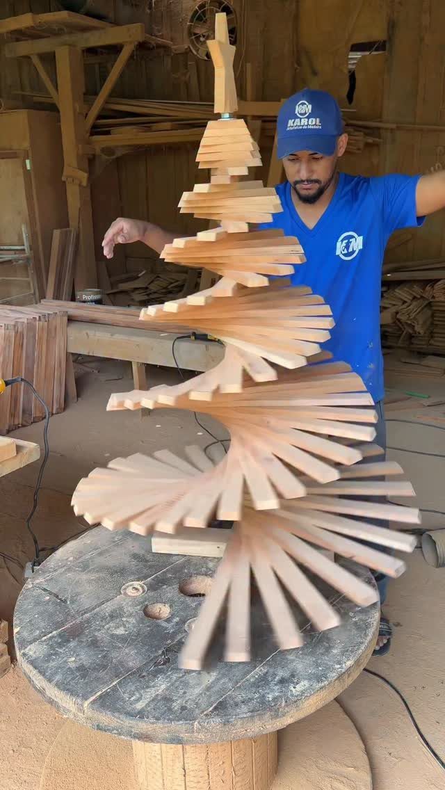 Make Wooden Christmas Trees: 7 DIY Projects from Scrap to Yard 6 A large spiral wooden Christmas tree sculpture sits on a round pedestal in a workshop.