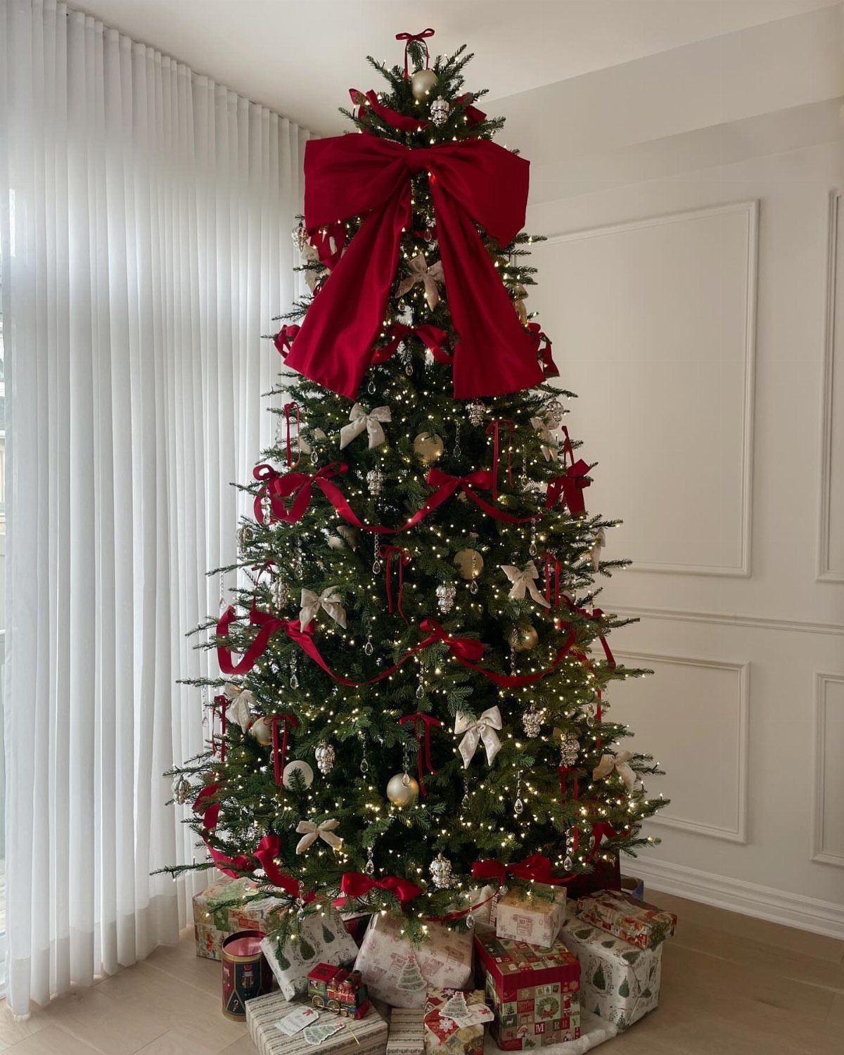 21 Most Beautiful Christmas Trees for Bold and Cozy Looks 6 A Christmas tree decorated with a large red velvet bow on top and red ribbons.