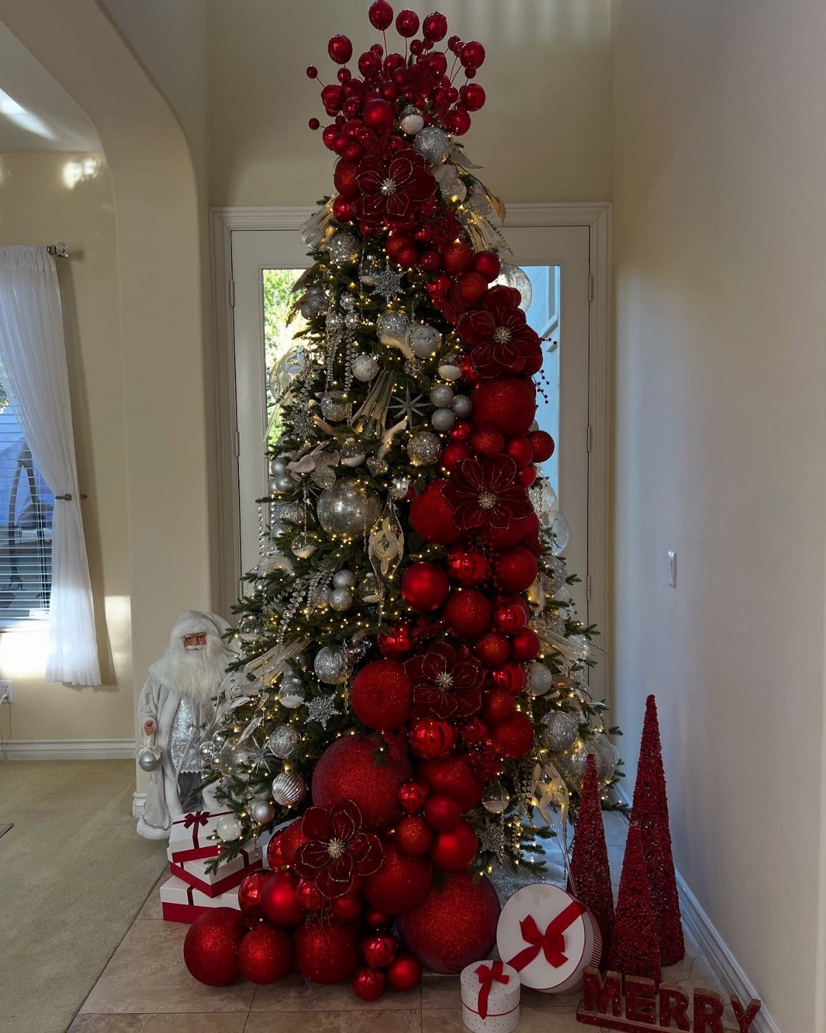 21 Most Beautiful Christmas Trees for Bold and Cozy Looks 1 A large Christmas tree decorated with many red and silver ornaments and red floral accents.