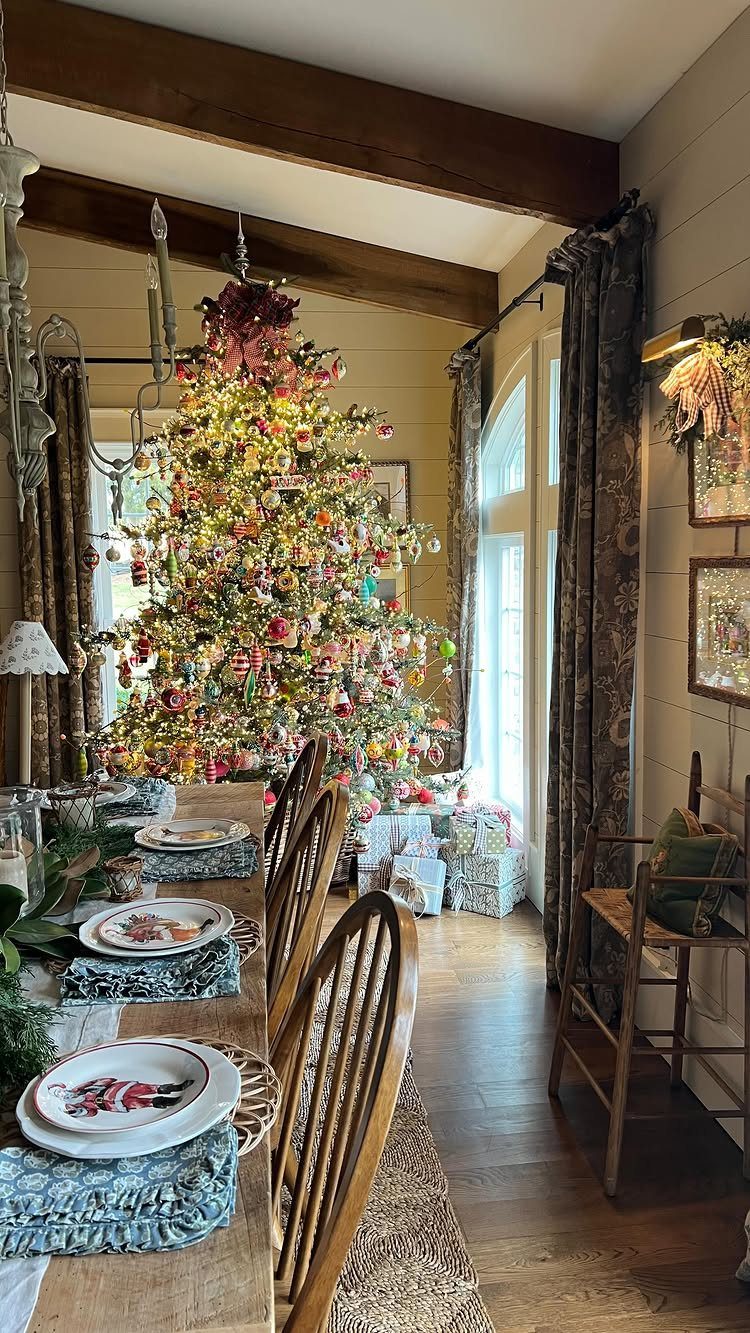 21 Most Beautiful Christmas Trees for Bold and Cozy Looks 9 Decorated Christmas tree with colorful ornaments standing in a dining room next to a set table.