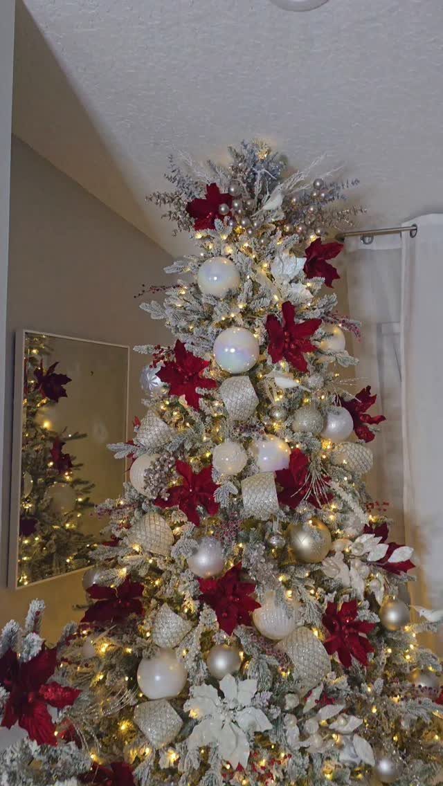 21 Most Beautiful Christmas Trees for Bold and Cozy Looks 15 A flocked Christmas tree decorated with red poinsettias, white ornaments, and warm lights.