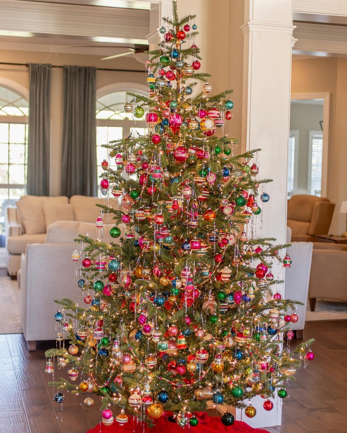 21 Most Beautiful Christmas Trees for Bold and Cozy Looks 7 A decorated Christmas tree with many colorful glass ornaments and glowing lights in a living room.