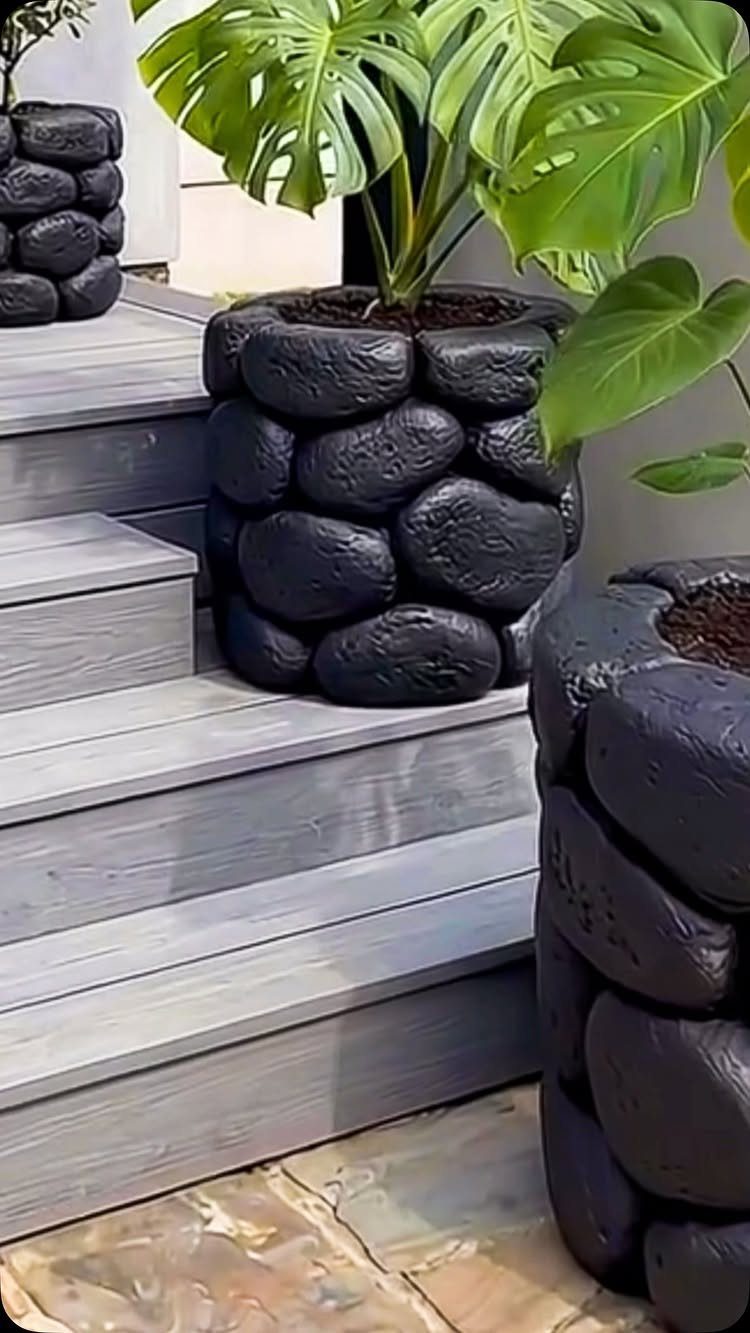 20 Plant Pot Ideas for Outdoor Spaces That Actually Work 13 Black stone-textured planters containing a large green Monstera plant on grey wooden steps.