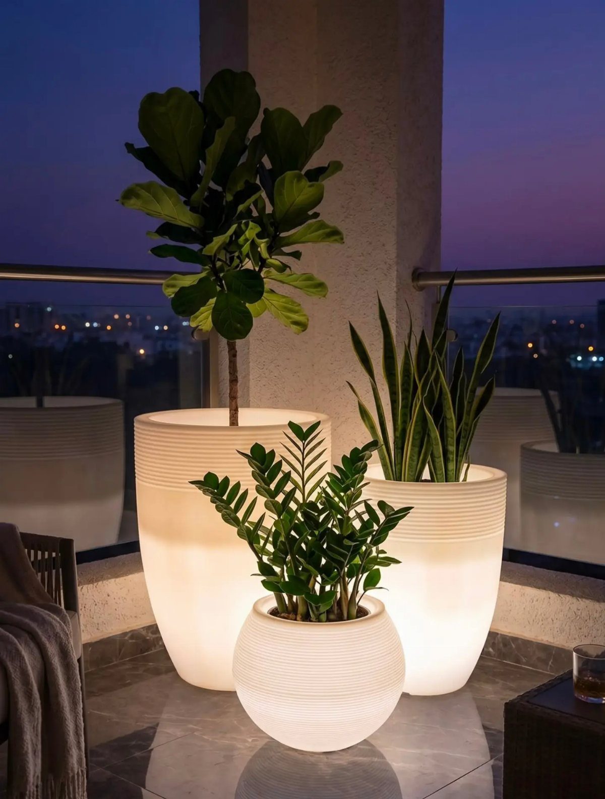 20 Plant Pot Ideas for Outdoor Spaces That Actually Work 14 Three glowing white ribbed planters with green leafy plants on a balcony at dusk.
