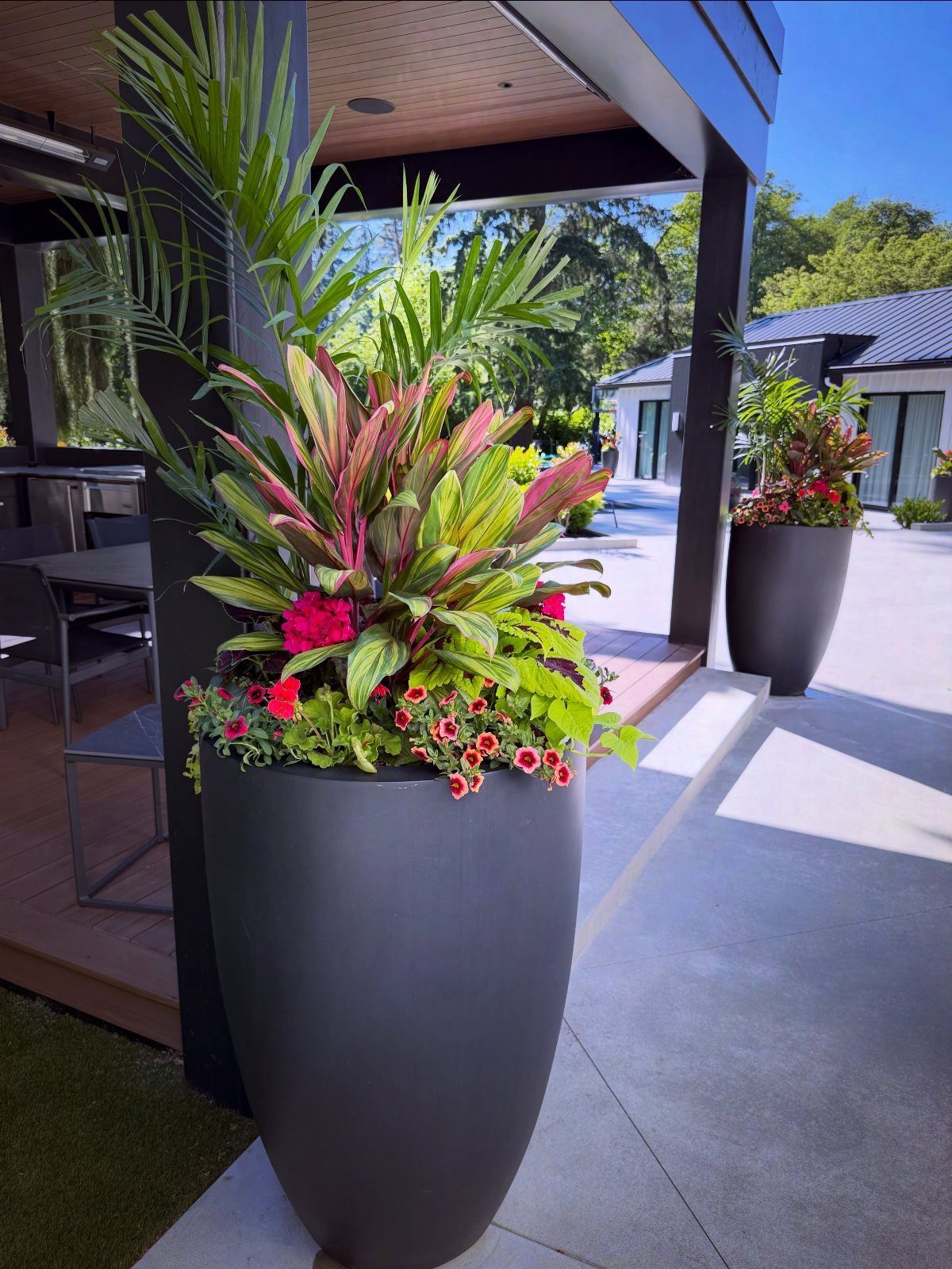 20 Plant Pot Ideas for Outdoor Spaces That Actually Work 20 Large dark grey planters filled with tropical green leaves and red flowering plants on a patio.