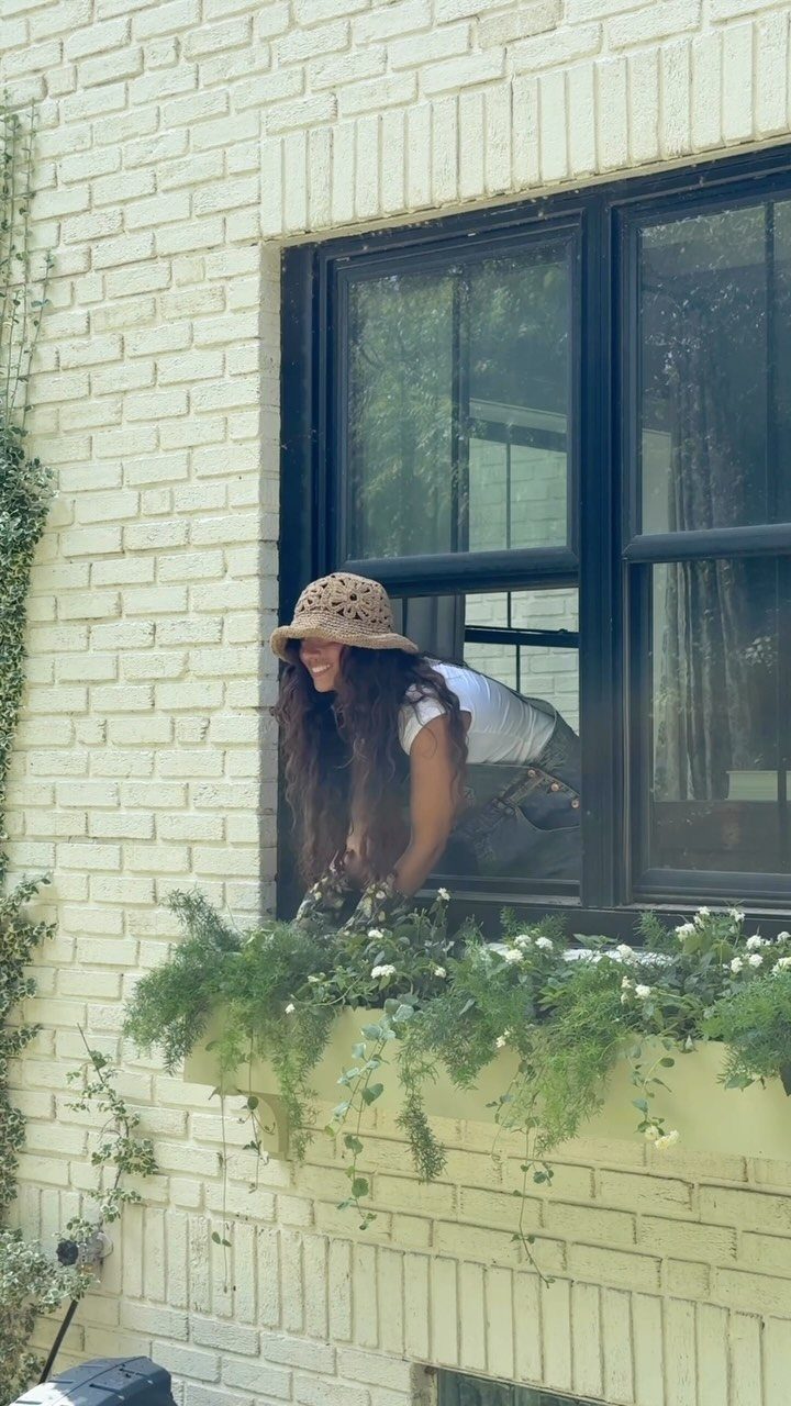 20 Plant Pot Ideas for Outdoor Spaces That Actually Work 5 A woman smiling behind a window with a flowering window box below.