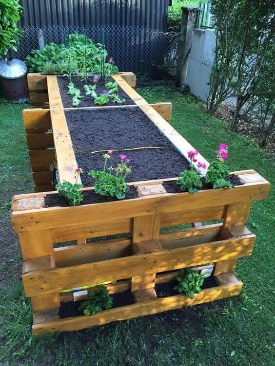 Raised Garden Beds for Small Spaces: 10 Ideas That Fit 7 A long raised garden bed made from wooden pallets filled with dark soil and small plants.