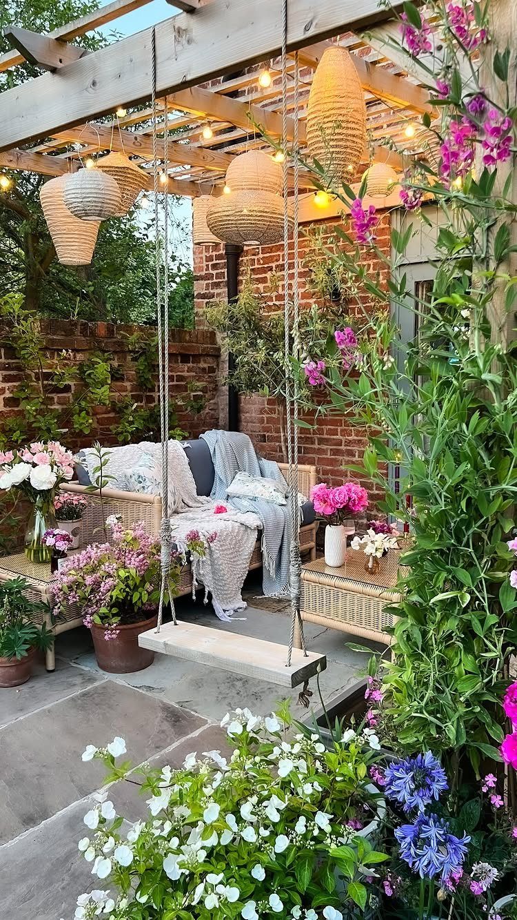 12 Small Backyard Design Ideas for Outdoor Living 10 A hanging wicker swing chair with pillows sits on a patio surrounded by blooming flowers and lanterns.