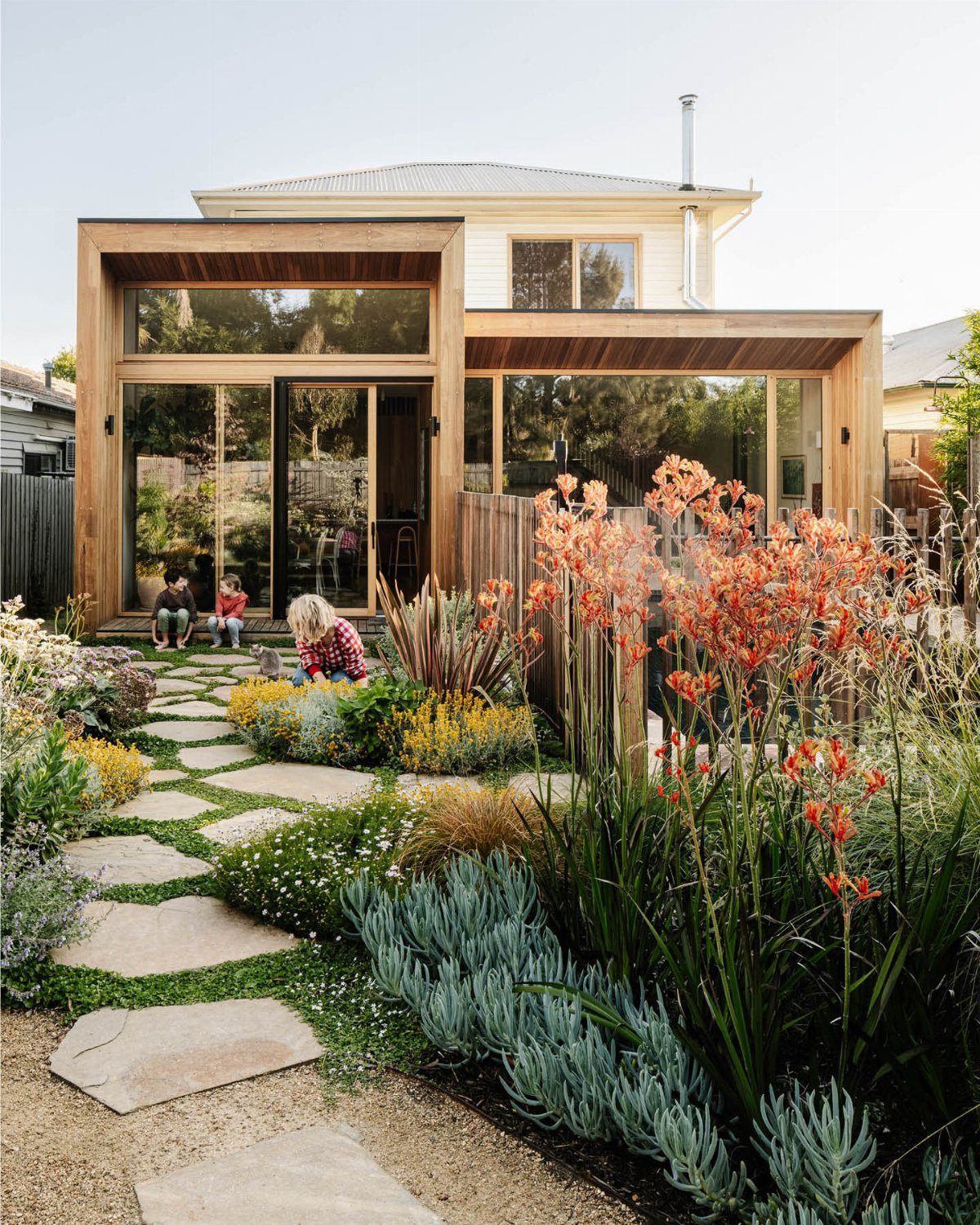 11 Small Flower Bed Ideas for Compact, Handsome Gardens 4 Orange kangaroo paw flowers and blue succulents grow along a stone path in a lush garden.