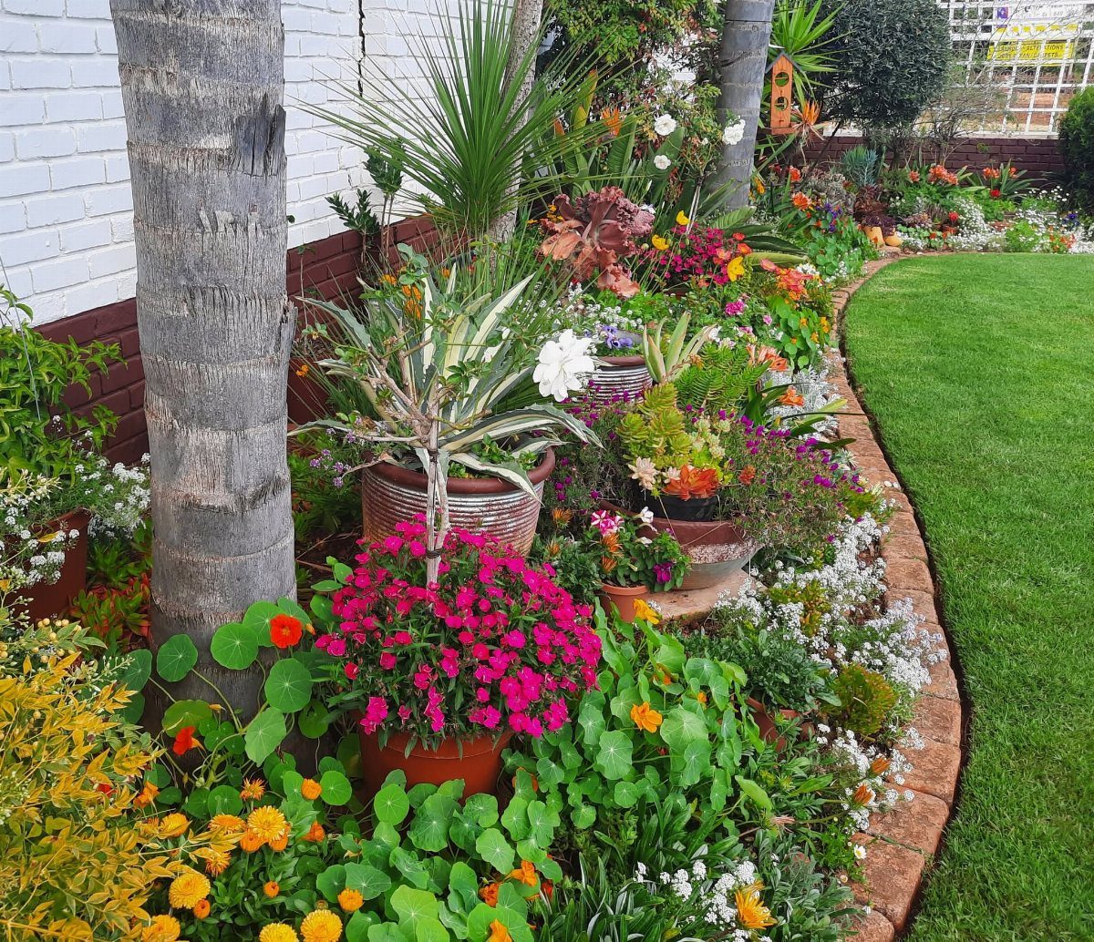 11 Small Flower Bed Ideas for Compact, Handsome Gardens 5 Colorful flowers and various potted plants arranged in a garden border next to a lawn.