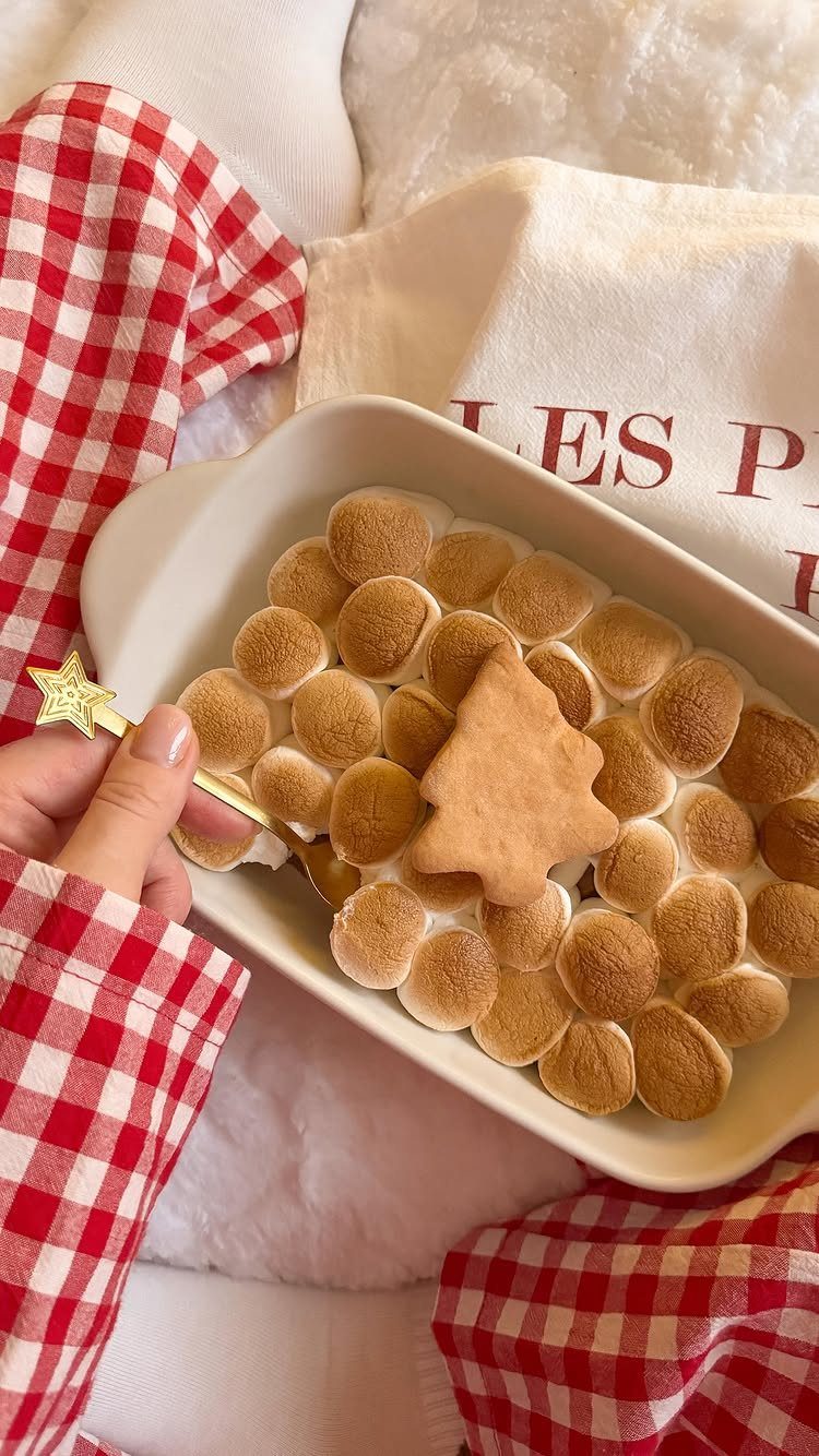 21 Things to Do for Christmas 2026 20 Person in checkered pajamas scooping toasted marshmallows with a gold star wand from a white dish.