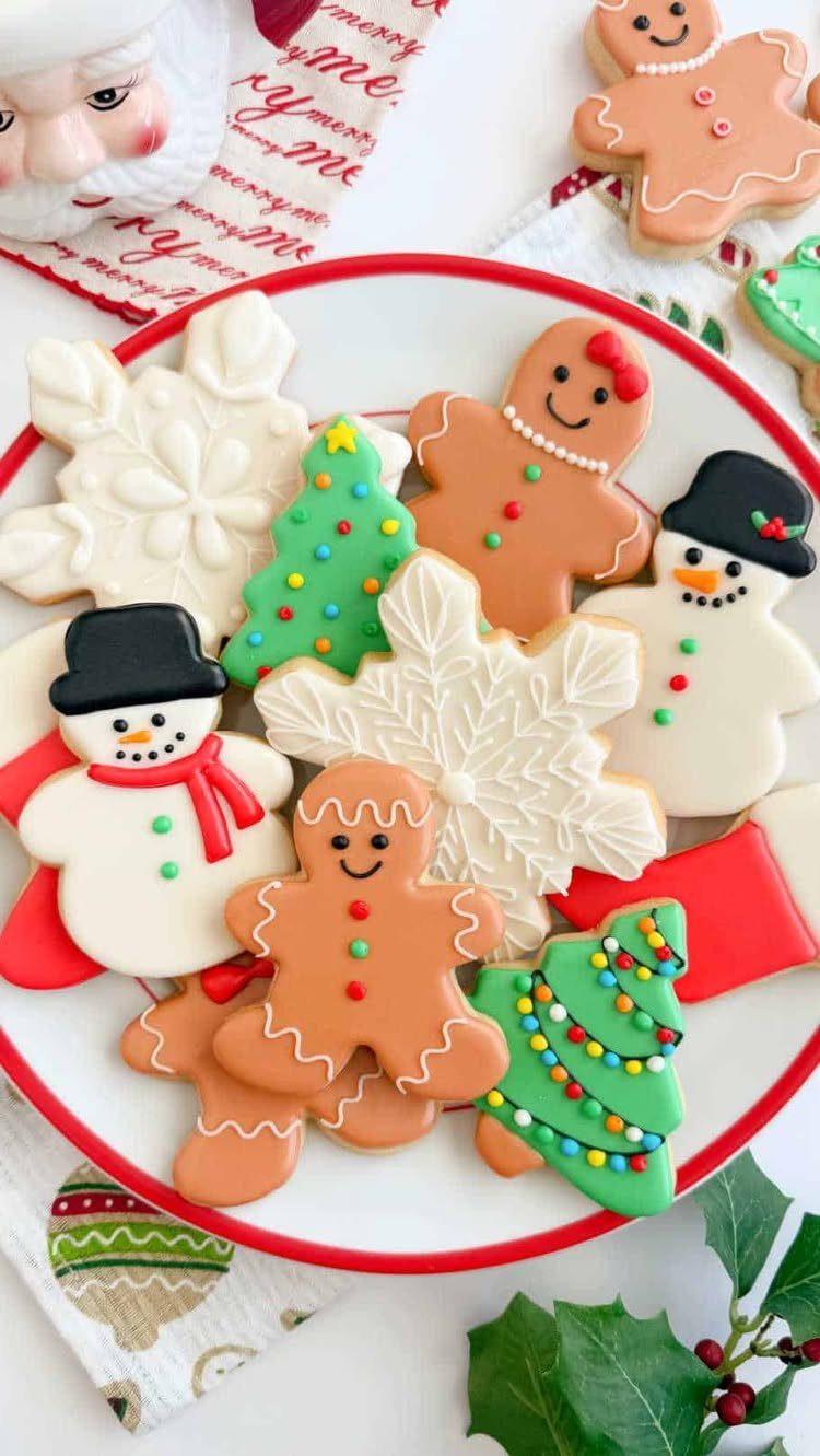 21 Things to Do for Christmas 2026 4 Decorated Christmas sugar cookies including gingerbread men, snowmen, and snowflakes on a red-rimmed plate.