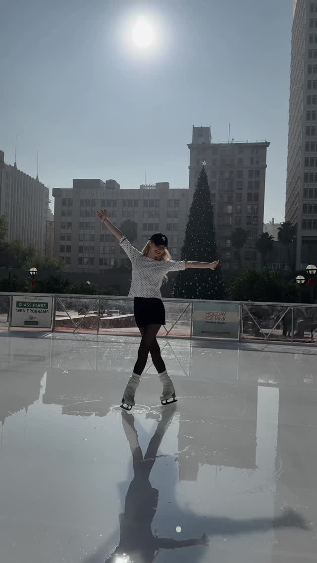 21 Things to Do for Christmas 2026 6 A woman ice skating on an outdoor rink with a Christmas tree and buildings behind her.