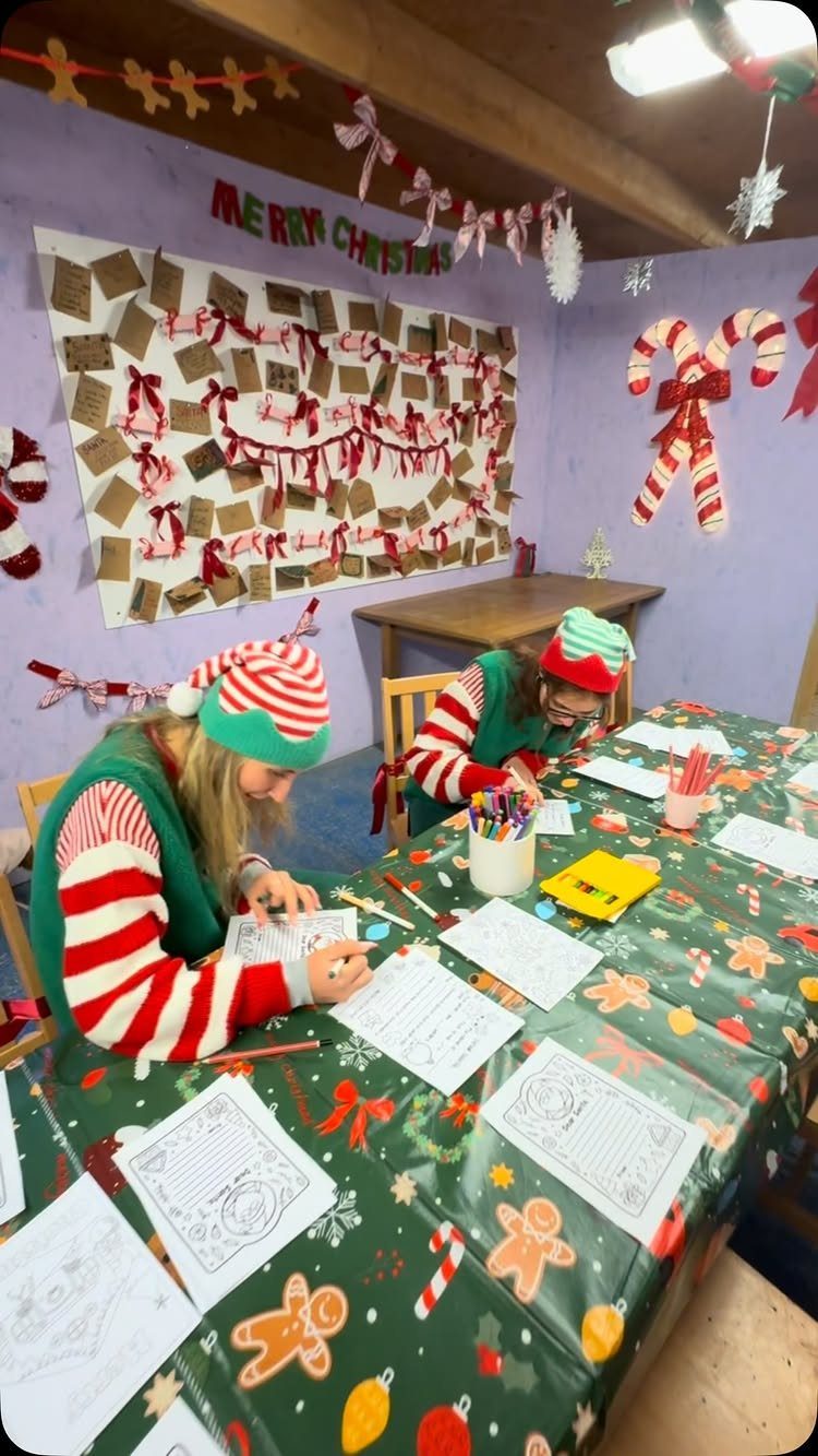 21 Things to Do for Christmas 2026 5 Two children in festive holiday clothing write letters at a decorated Christmas table.