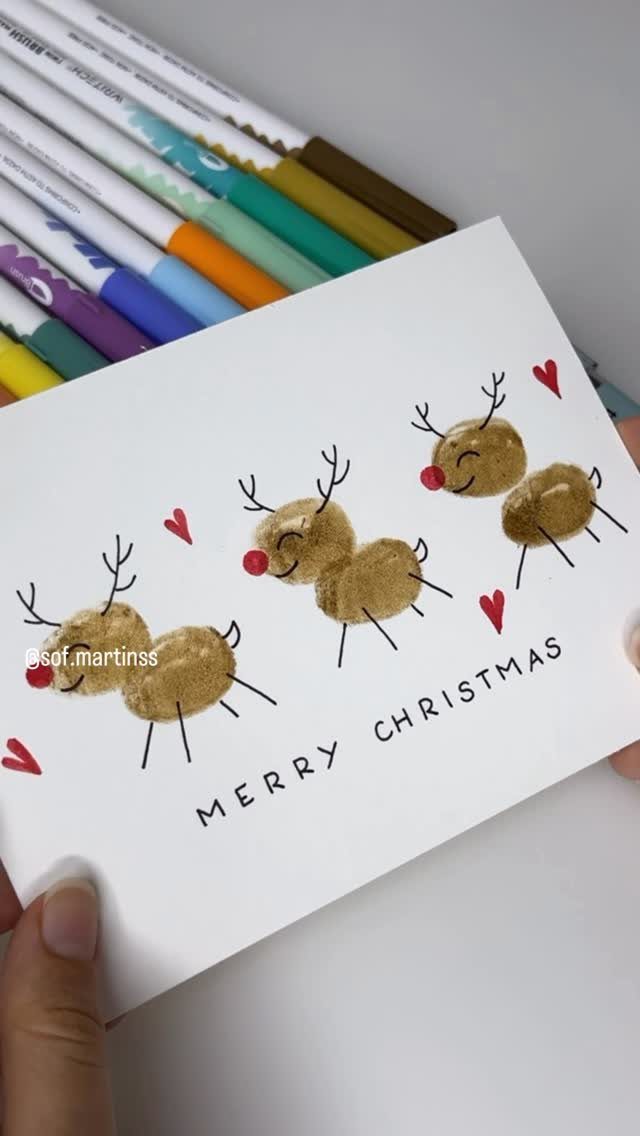 21 Things to Do for Christmas 2026 16 Hand holding a white Christmas card decorated with three gold reindeer and red hearts.