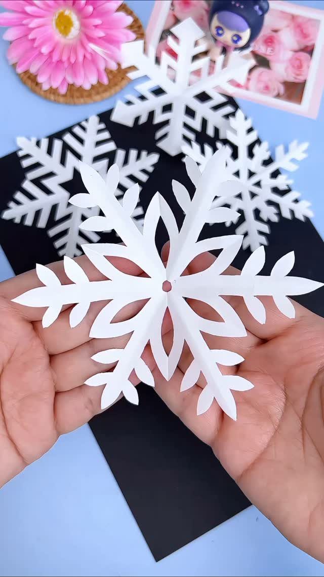 21 Things to Do for Christmas 2026 15 Hands holding a large, intricately cut white paper snowflake over black paper.