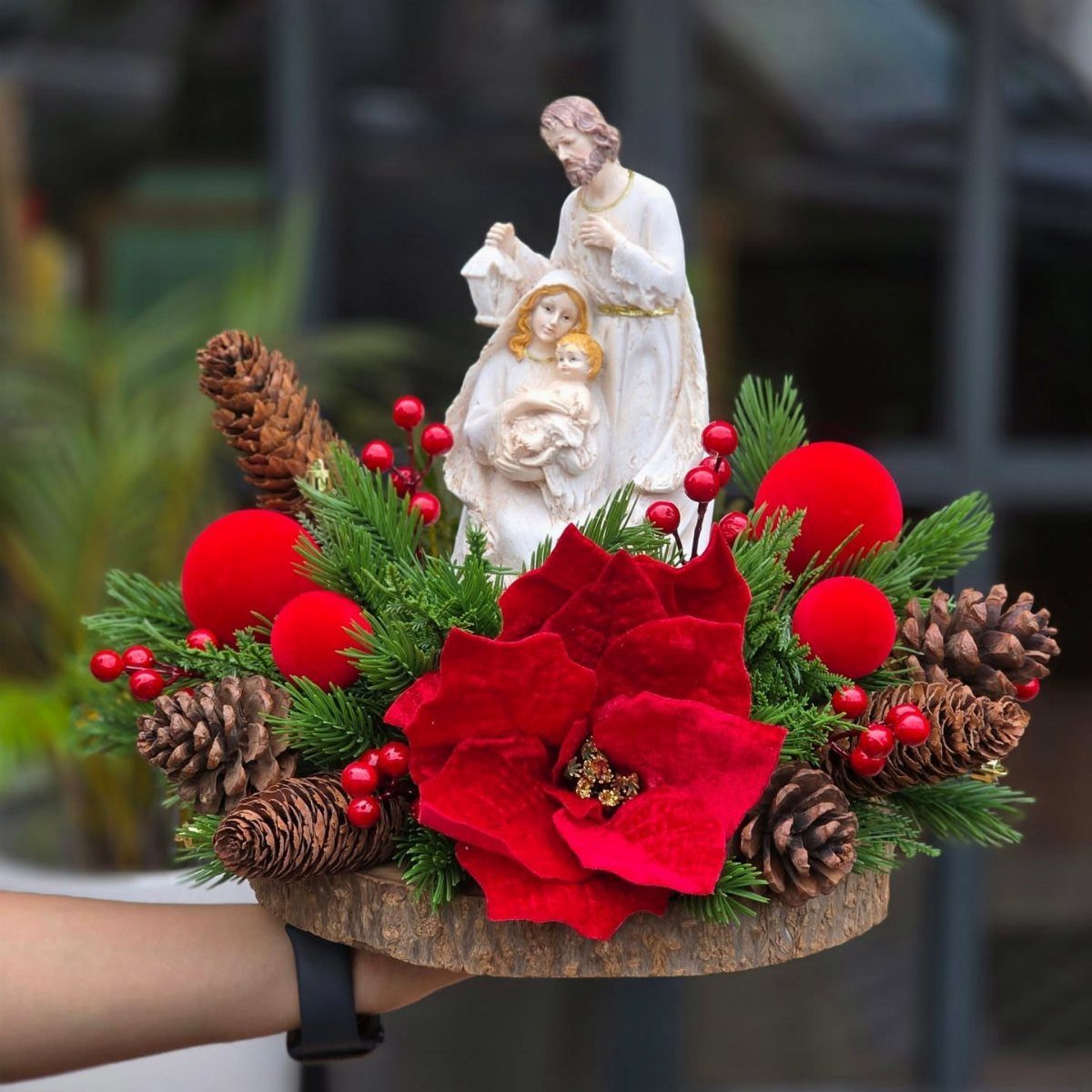 21 Things to Do for Christmas 2026 13 A nativity scene figurine surrounded by red poinsettias, pinecones, and greenery on a wooden base.