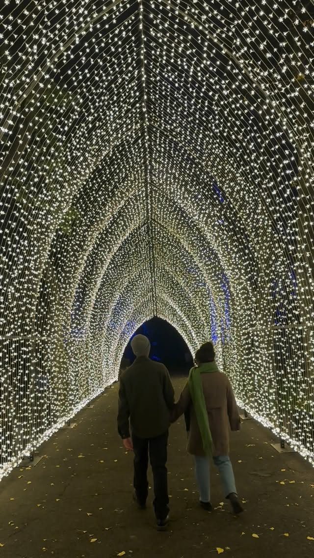 21 Things to Do for Christmas 2026 1 Two people walking through a glowing tunnel of white Christmas lights at night.