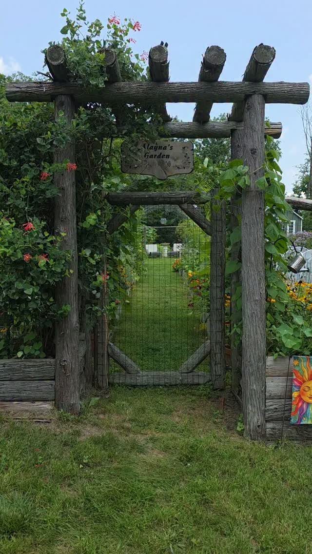 7 Vegetable Garden Ideas for Small Spaces and Big Harvests 7 A rustic wooden log pergola gate decorated with climbing green vines and pink flowers.