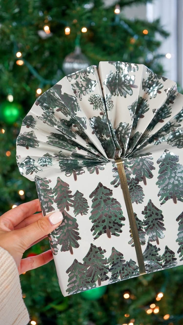 Winter and Christmas: 3 Ways the Season Gathers People 3 A hand holding a wrapped Christmas gift with silver tree patterns and a large pleated bow.